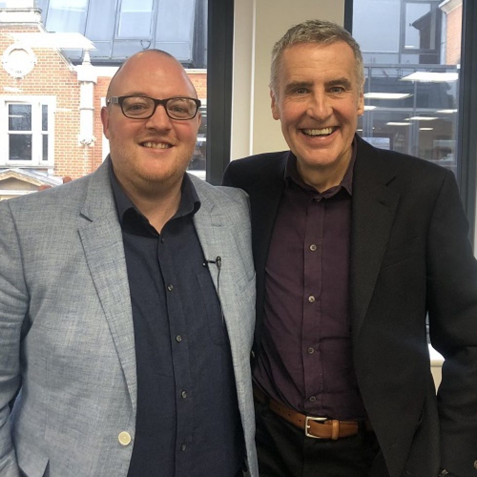Dermot Murnaghan in a burgundy shirt and black jacket on the right standing with his arm around News Associates head of journalism Andrew Greaves in a dark blue shirt and light blue jacket. They both have big grins on their faces.