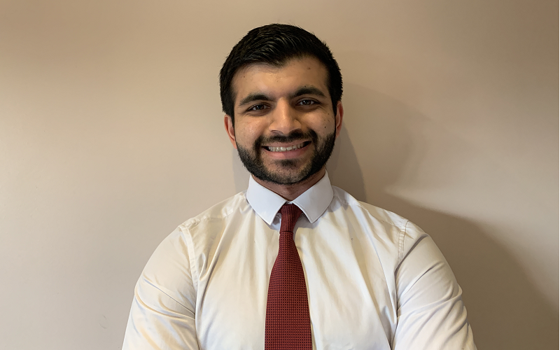 Kumail Jaffer smiling in a white shirt and red tie against a white wall