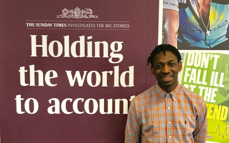 NCTJ-accredited grad Shingi in front of a sign that reads 'Holding the world to account'.