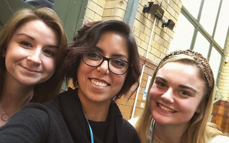 A selfie of Lucy Dyer, Laura Garcia and Emma Bentley. The selfie is taken by Laura in the middle. Lucy is on the left and Emma is on the right. The shot is quite close so you can only see their faces. They are all smiling. The three women all look different - Lucy is smiling with her lips closed, she has white skin and brown hair. Laura has a lovely toothy grin, a beautiful Mexican complexion, short dark hair and black glasses. Emma's blonde hair is pushed back with a leopard skin patterned head band, she has pale skin and a big grin.