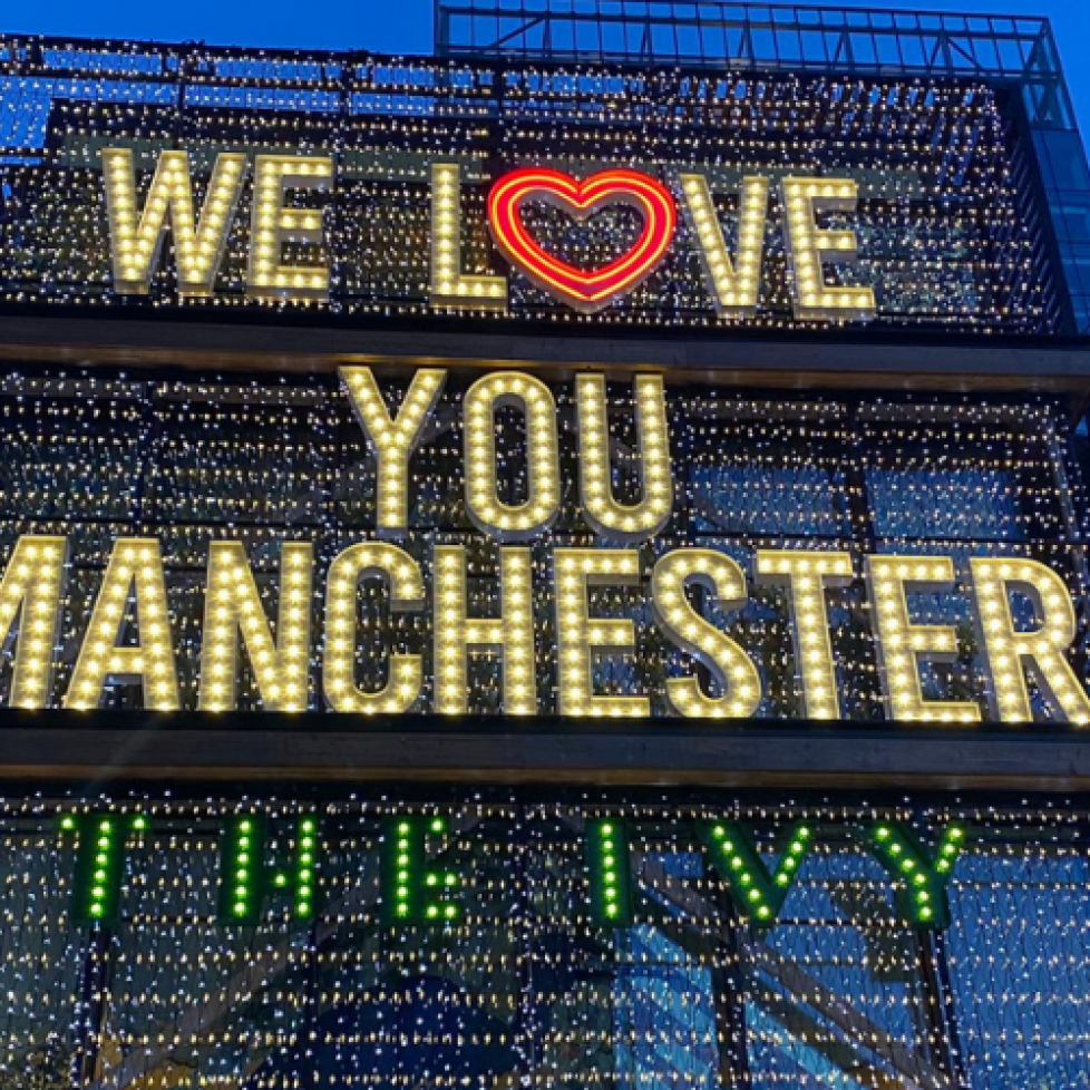 Photo of We Love You Manchester sign outside the Ivy, lit up with a loveheart replace the o in love
