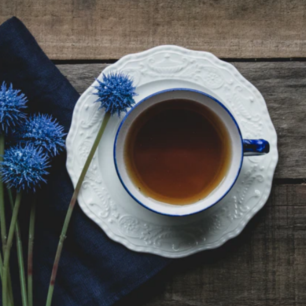 Stock image of a cup of tea on a wooden table, view from above. A few blue flowers placed to the left of the mug.