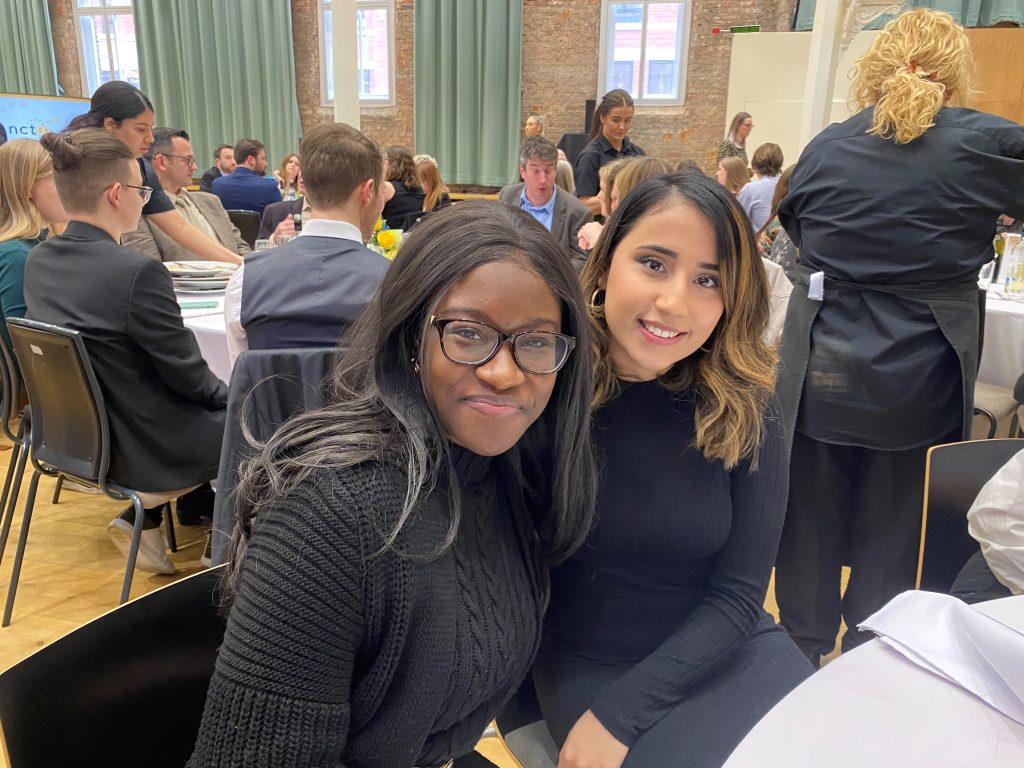 News Associates London fast-track graduates Phoebe and Neha smiling at a table at the NCTJ awards.