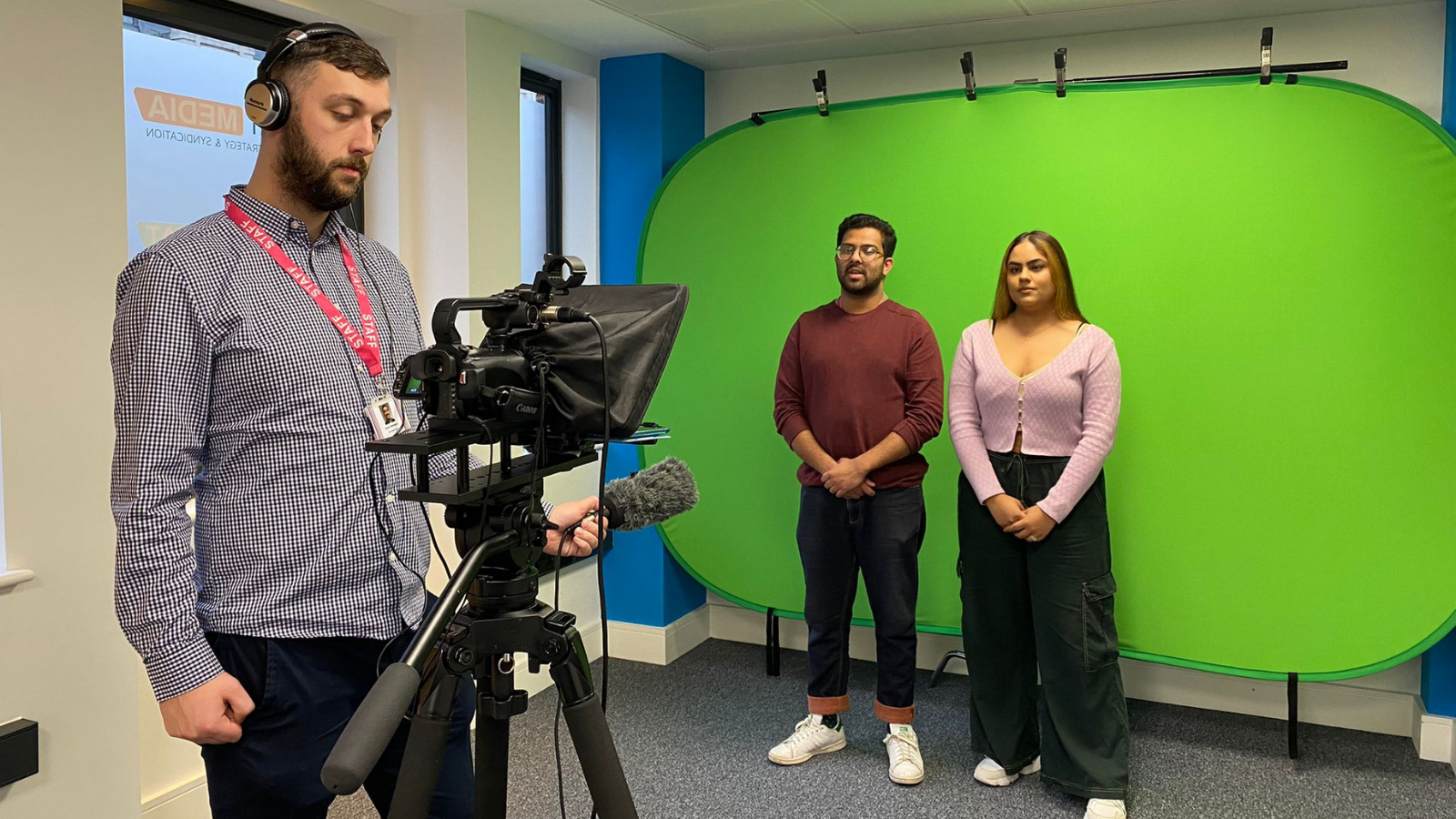 Trainees and a tutor doing a news bulletin exercise in front of a camera and autocue and with a green screen backdrop 