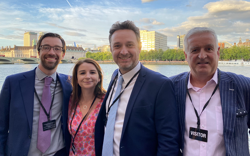 News Associates staff Graham Moody, Lucy Dyer, James Toney and Graham Dudman all dressed up at the House of Lords. They are standing outside on the terrace with the Thames and London as their backdrop. It’s a beautiful sunny evening with a lovely blue sky. The men are all wearing smart suits and Lucy is wearing a pink dress. They are all smiling with their arms around each other. The photo was taken after our remote journalism course was accredited.