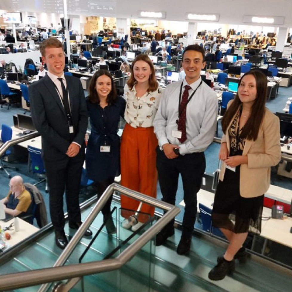 Five Telegraph editorial graduates standing in front of the newsroom. They are all dressed smart and smiling.