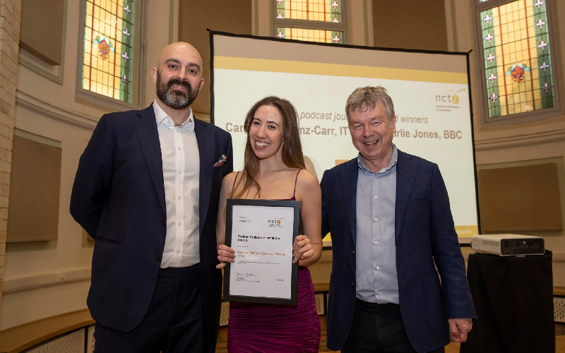 Carolina collecting her NCTJ Award for Excellence for trainee podcast. Carolina is holding her framed A4 certificate standing between Mark Hudson and Nick Powell who presented the award. All three are dress smarty and smiling.