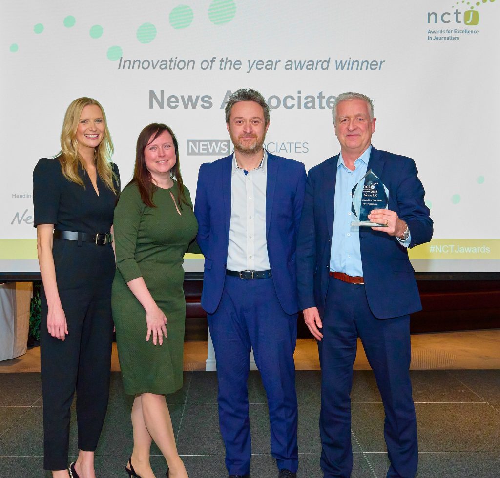 News Associates managing editor James Toney (centre right) and deputy managing editor Graham Dudman (right) collecting the innovation of the year award from Sky Sports News presenter Jo Wilson (left) and Financial Times deputy managing editor Abbie Scott (centre left). They are all standing and smiling for the camera. They are all smartly dressed. Graham Dudman is holding the glass award. 