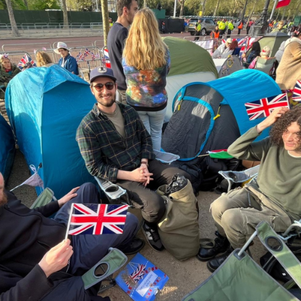News Associates trainees camping out in London to cover the coronation. They're sitting it camping chairs surrounded by tents waving Union flags.
