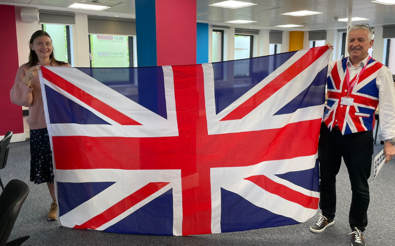 Eliza and News Associates deputy managing editor Graham Dudman holding a massive Union flag for the coronation. Graham is also wearing a Union flag waistcoat.