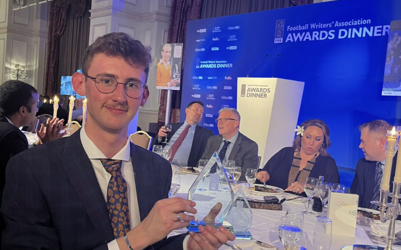 A photo of News Associates sports journalism trainee Dom Smith holding his Football Writers' Association Hugh McIlvanney Student Football Writer of the Year award.