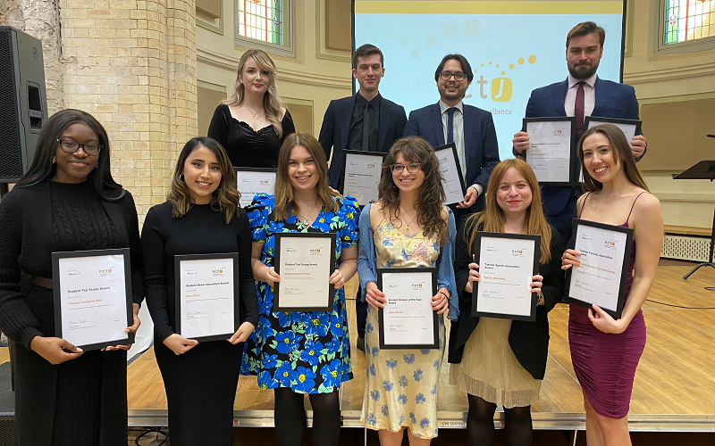 News Associates NCTJ Awards for Excellence 2021 shortlisted and winning graduates. The ten graduates are standing in two lines on the stage. Everyone is dressed smartly and are smiling at the camera holding their framed certificates.