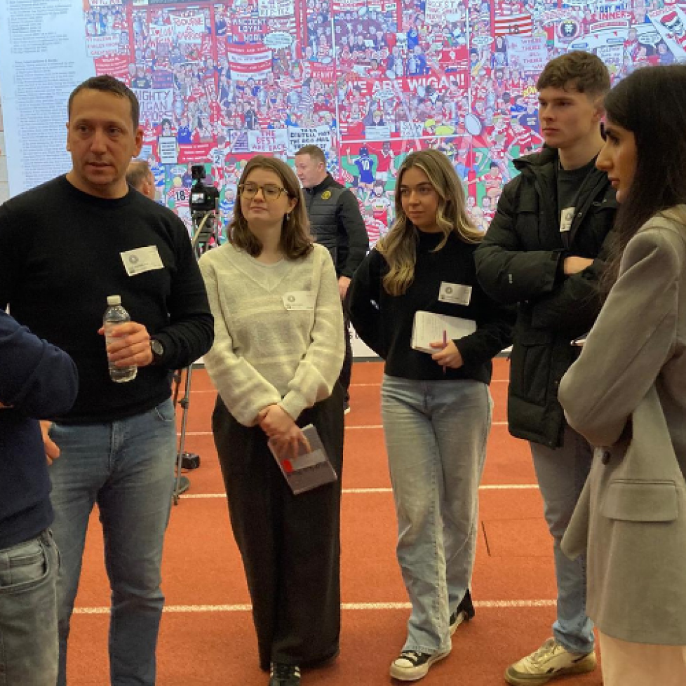 Four News Associates trainees with notebooks to hand (pictured right) and tutor Phil Wilkinson in conversation with a Wigan Warriors representative at The Brick Community Stadium.
