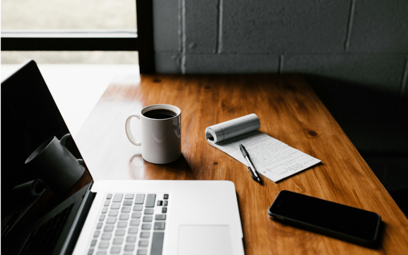 A photo of a desk with a laptop, notebook and cup of coffee on. The image is being used to illustrate an article titled How to prepare for a News Associates course.